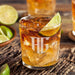 Personalized whiskey glass displayed with whiskey, ice, and fresh lime on a rustic wooden surface. The engraved monogram and year design stands out clearly.