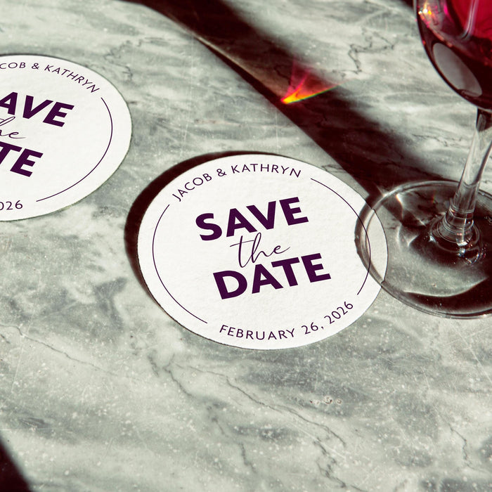 Personalized Save the Date coaster displayed beside a wine glass. Modern wedding favor customized with names and wedding date.