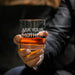 Close-up lifestyle photo of a whiskey glass held in hand, featuring the “Ask Your Mother” engraving. The glass is filled with whiskey and ice, perfect for gifting.