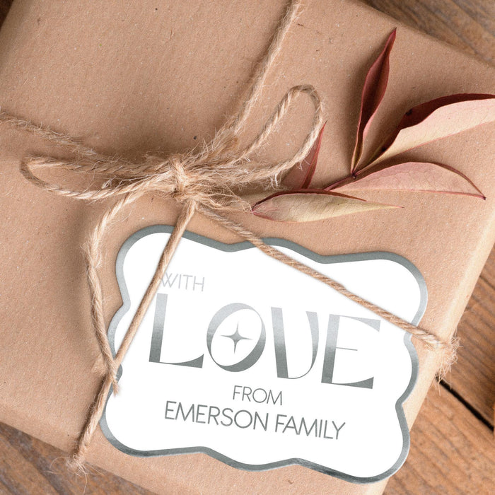 Close-up of a metallic silver “With Love” wedding gift tag tied onto blush fabric wrapping with twine. The personalized foil cardstock tag features a modern script design and custom sender name.