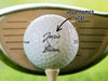 Titleist golf ball is shown sitting on a golf tee with a golf club behind it. Ball features custom printed Newlyweds&#39; Names Design. Text says: Your Names Here.