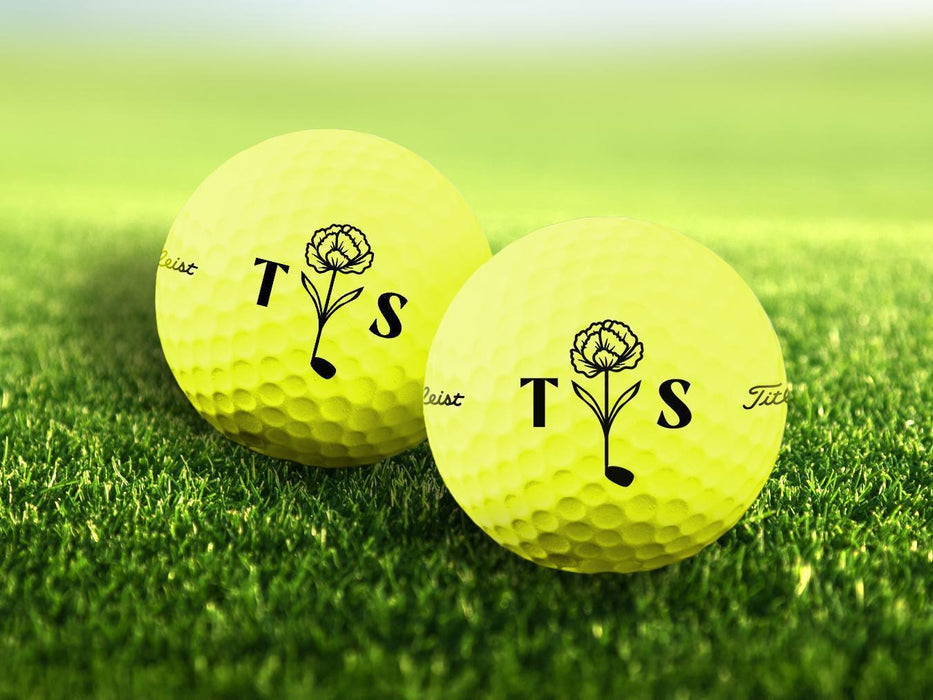 Two personalized yellow golf balls with a Floral Initial Monogram design printed on them, placed on a grassy field.