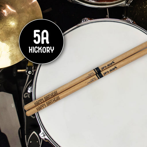 A pair of drumsticks with the text "Happy Birthday" engraved on them, placed on a drum set.