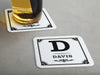 One coaster has a drink on it and an empty coaster sits beside it. Coasters say Davis with decorative frame.