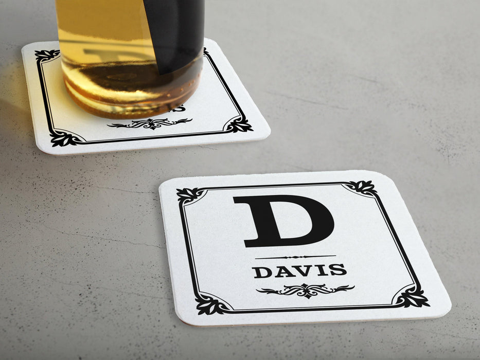 One coaster has a drink on it and an empty coaster sits beside it. Coasters say Davis with decorative frame.