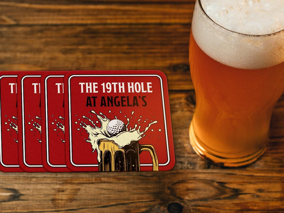 Custom square pulpboard coasters are shown sitting on a wooden table with a pint of beer beside them. The custom coasters feature a 19th hole bar design with an illustration of a golf ball splashing into a beer mug and a red background.