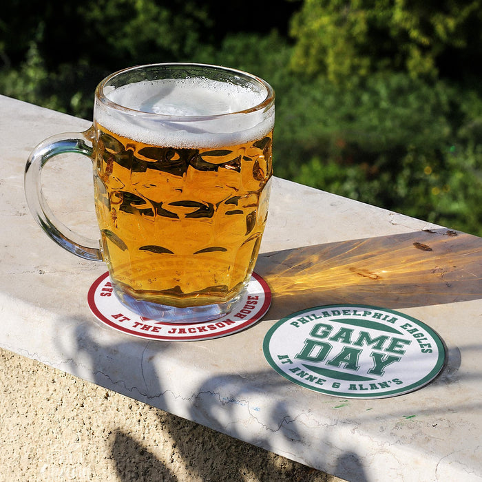 Personalized football coasters shown outdoors with a beer mug, featuring custom team wording and family names.