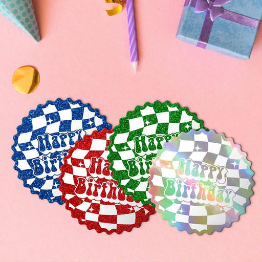 Four groovy birthday gift tags in metallic rainbow, glitter blue, glitter green, and glitter red lying beside colorful gifts and party decorations.