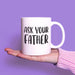 White ceramic mug balanced on an open hand against a purple background. A clean product-focused image that highlights the bold black design clearly.