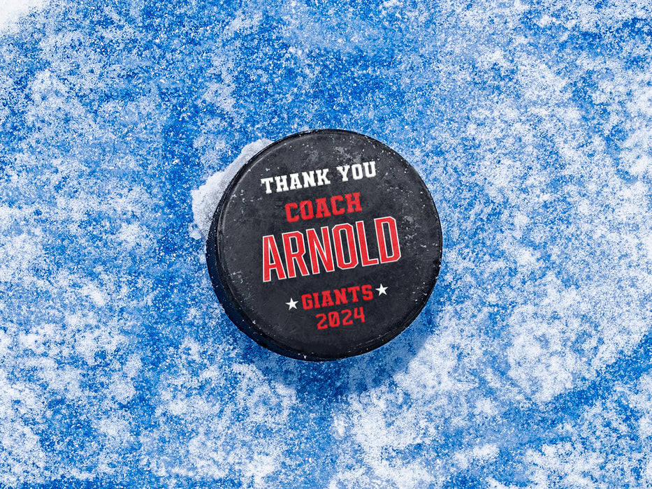 single hockey puck on blue ice rink with a red coach appreciation design that says Thank You Coach Arnold, Giants, 2024