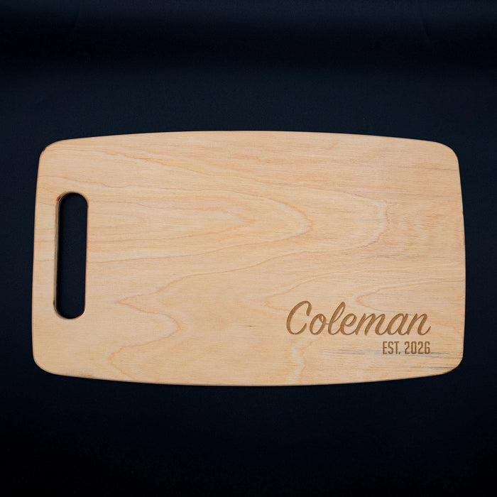 Full view of the personalized maple cutting board engraved with Coleman and EST. 2026 on a dark background.