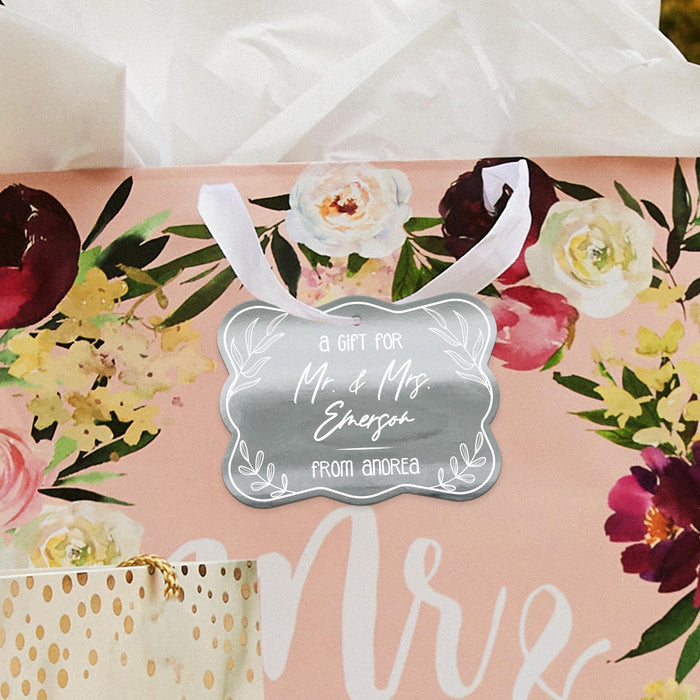 Romantic floral flat lay featuring a personalized “Mr. & Mrs.” wedding gift tag in metallic silver foil. Styled with flowers and soft wedding décor for bridal shower and wedding inspiration.