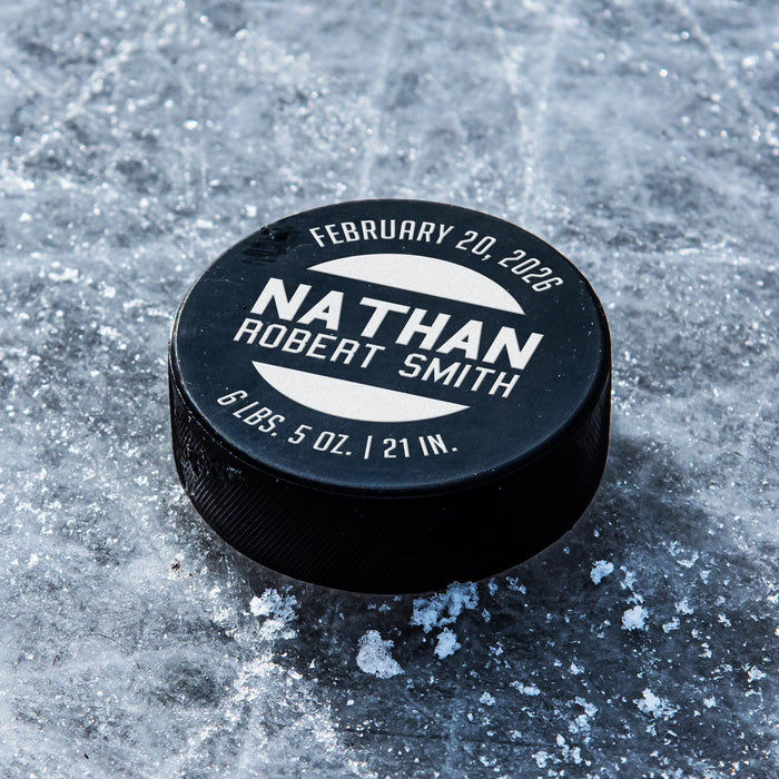 Personalized black hockey puck with a white UV printed birth announcement design featuring the baby’s name, birth date, weight, and length.