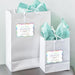 White gift bags with tissue paper featuring personalized “Let Your Adventure Begin” wedding gift tags on holographic rainbow foil. Styled as elegant wedding welcome bag and favor packaging ideas.