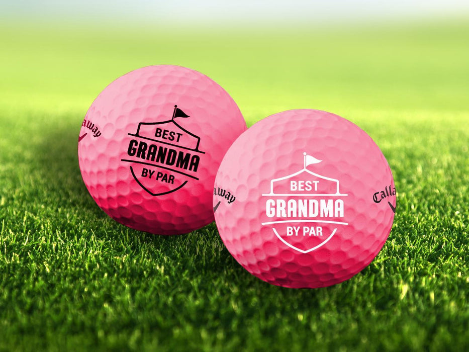 Two golf balls with the phrase "Best Grandma By Par" design printed on them, placed on a grassy field.