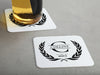One coaster has a drink on it and an empty coaster sits beside it. Coasters say Collins Est. 2017 with laurel design.