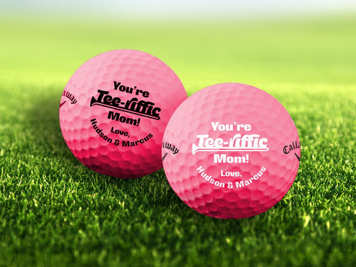 Two golf balls with Tee-Riffic design printed on them, placed on a grassy field.