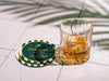 Custom square pulpboard coaster are shown laid out on marble floor. A whiskey glass is shown next to the coaster. The custom coasters feature design printed with script and serif customizable text and striped background.