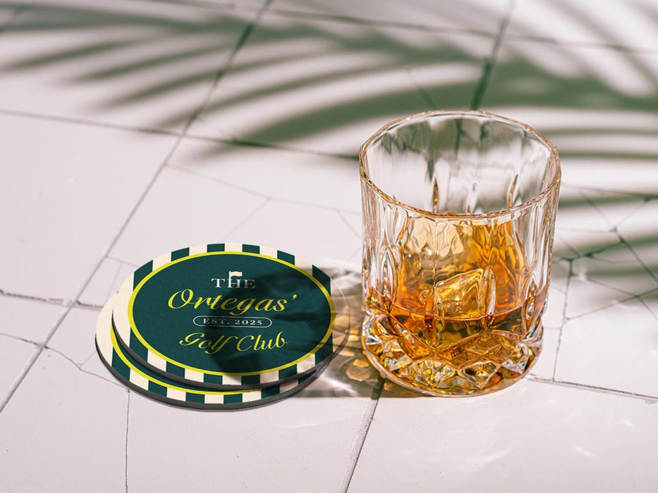Custom square pulpboard coaster are shown laid out on marble floor. A whiskey glass is shown next to the coaster. The custom coasters feature design printed with script and serif customizable text and striped background.