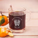 A glass mug filled with a dark liquid, likely coffee, sits on a wooden surface. The mug has a personalized message engraved on it, celebrating Father's Day with the year "2026" and the names "LOVE, REED".