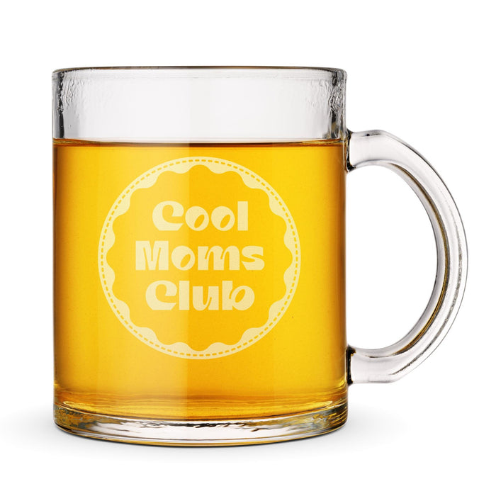 A glass mug filled with a yellow liquid, likely beer, with the text "Cool Moms Club" engraved on it.