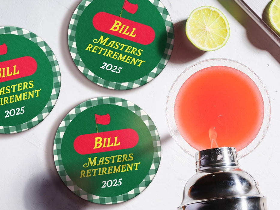 Custom round pulpboard coasters are shown sitting on a white marble surface next to lemons and an azalea cocktail being poured from a silver cocktail shaker. The coasters read Bill Masters Retirement 2025. These feature a red, green, and yellow Masters-themed retirement party design with the retiree’s name and retirement date.