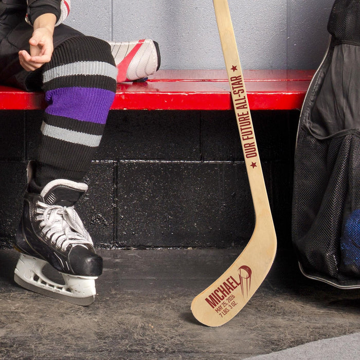 Lifestyle image of a hockey player in skates holding a personalized mini hockey stick with baby name and birth info printed on the blade.