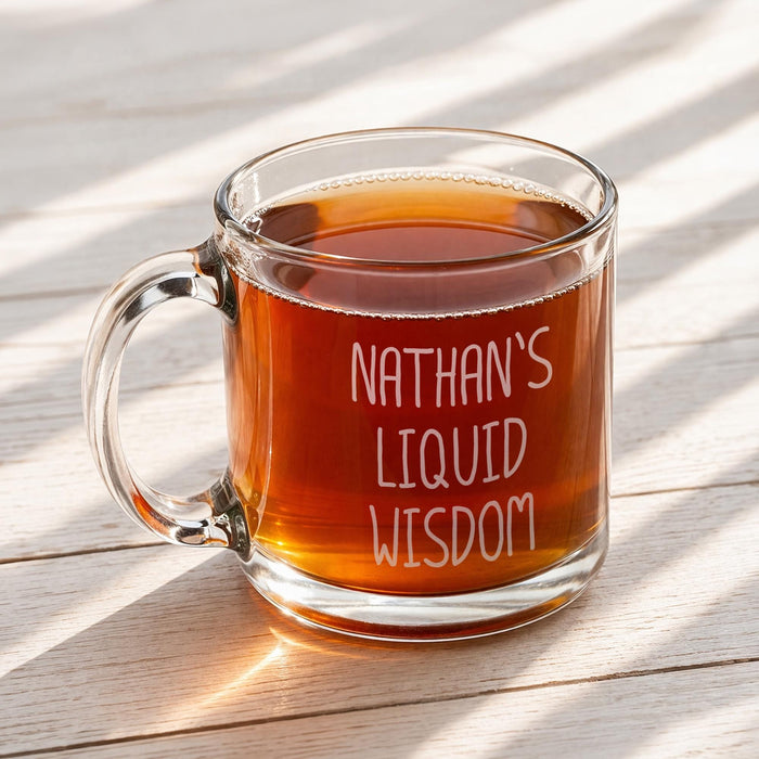 A glass mug filled with a brown liquid, likely tea, sits on a wooden surface. The mug has the text "NATHAN'S LIQUID WISDOM" engraved on it.