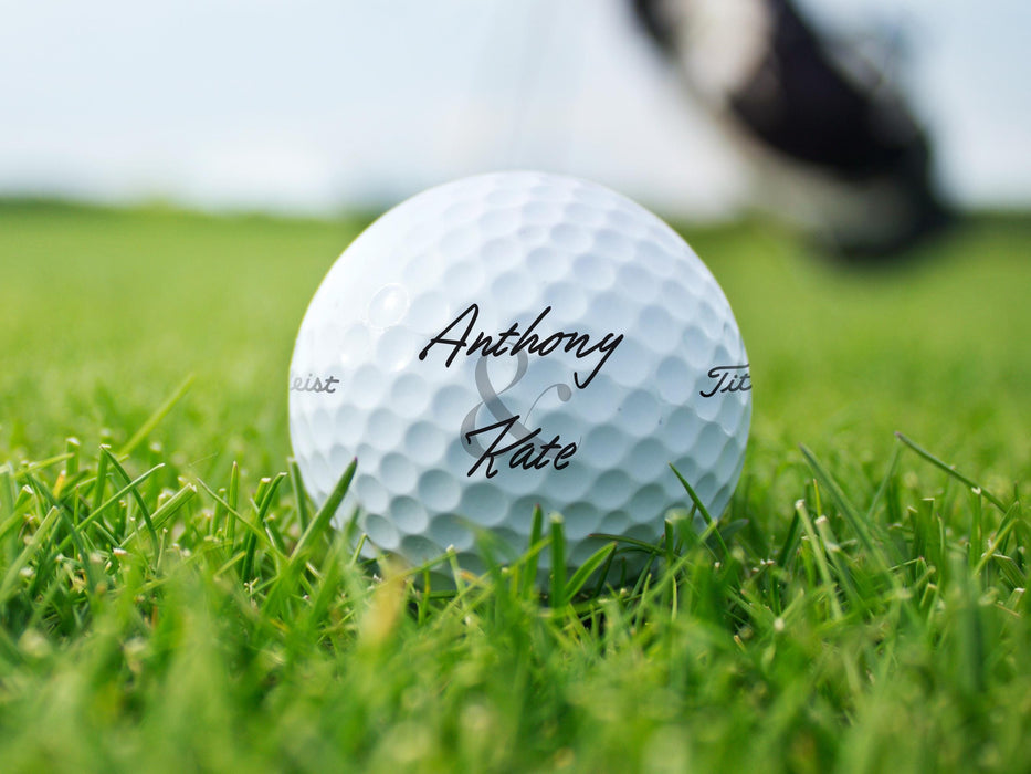 Titleist golf ball is shown sitting on grass. Ball features custom printed Newlyweds&#39; Names design.