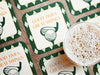 Custom square pulpboard coasters are shown laid out on a wooden surface. A beer mug is shown on top of a few of the coasters. The coaster features design with an illustration of a golf ball and with club behind it, argyle background pattern, and custom text.