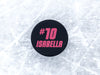 single hockey puck on ice rink with name and number design printed in pink that says Isabella number 10