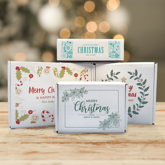 Personalized Christmas golf ball gift boxes displayed in a festive holiday setting, featuring four printed Christmas designs with custom messages.