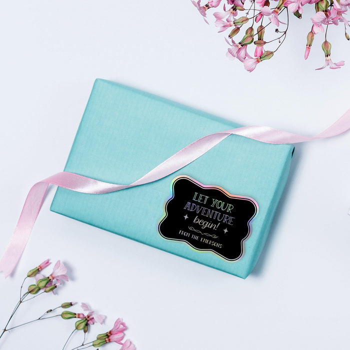 Small pastel gift box wrapped with ribbon and decorated using a rainbow foil “Let Your Adventure Begin” wedding gift tag. A modern and colorful presentation idea for wedding favors and gifts.