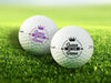 Two golf balls with the text "Queen of the Green" printed on them, placed on a grassy field.