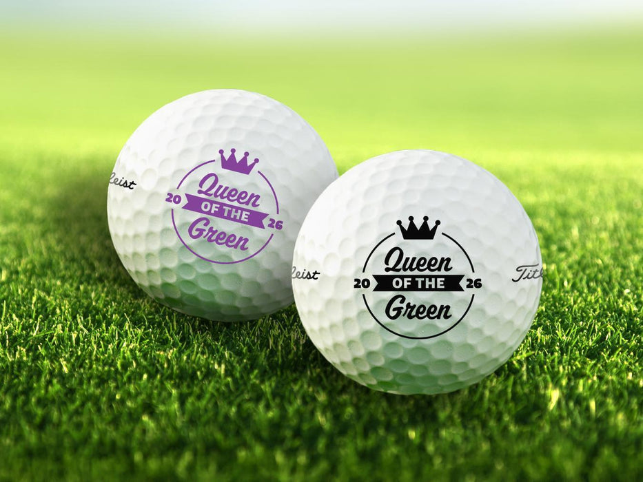Two golf balls with the text "Queen of the Green" printed on them, placed on a grassy field.