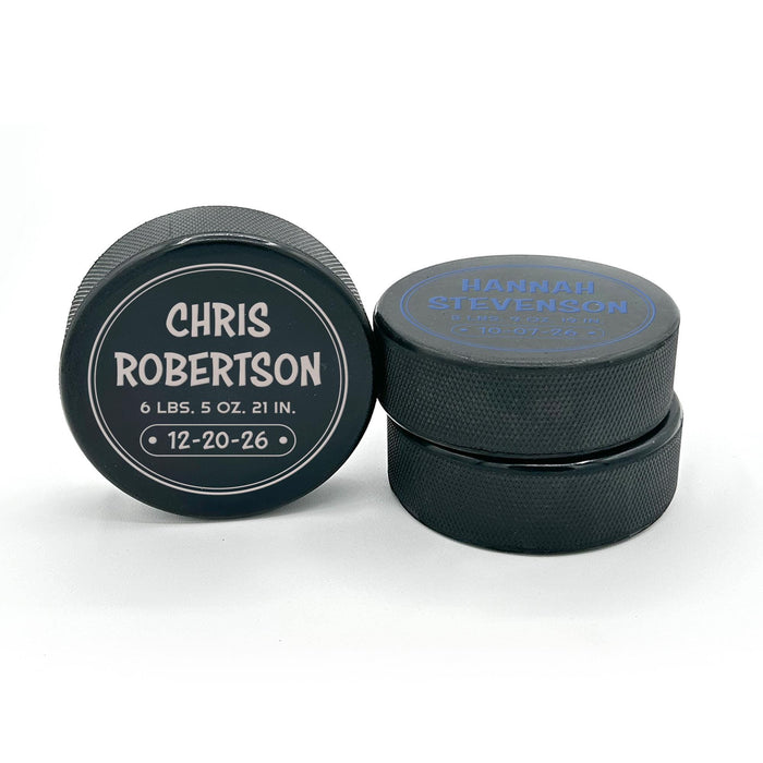 Two personalized hockey pucks showing the UV printed birth announcement design from the front and side.