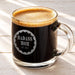 A mug of dark coffee with a foam top, sitting on a wooden surface.