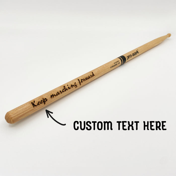 A wooden drumstick with the text "Keep marching forward" engraved on it, along with an arrow point toward it with the words "CUSTOM TEXT HERE" written next to it.