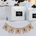 Silver gift bag decorated with a personalized “Your Biggest Fans” wedding gift tag in metallic silver foil. Styled with wedding décor and hanging banner accents for a romantic presentation.