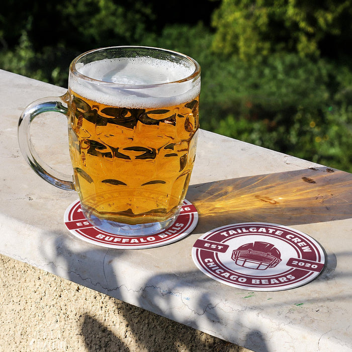 Personalized Tailgate Crew football coasters displayed outdoors with a glass of beer, showing custom team names and game day colors.