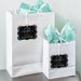 White gift bags with tissue paper featuring personalized “Let Love Sparkle” foil wedding gift tags. A modern and elegant presentation idea for wedding welcome bags and favors.
