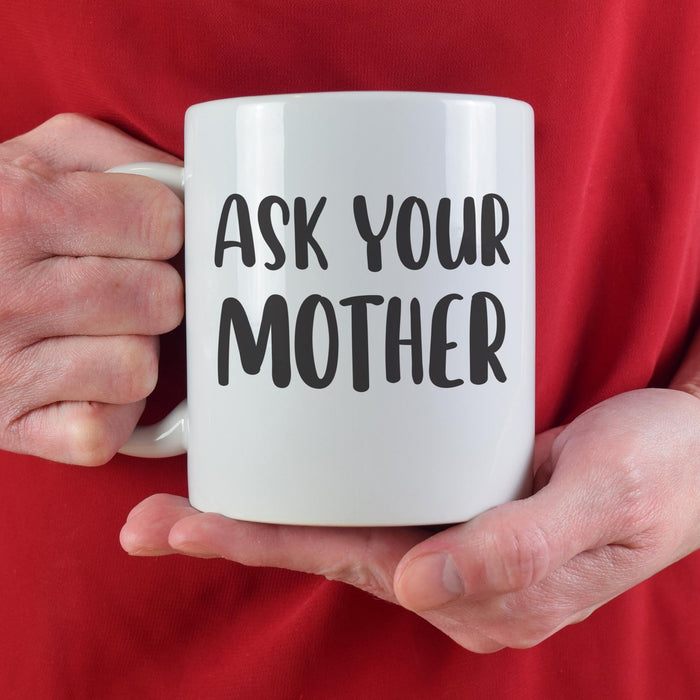 A person in a red sweater holding the “Ask Your Mother” mug with both hands. The cozy lifestyle setting adds warmth and playful gift appeal.
