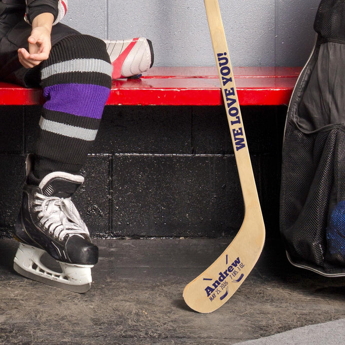 Lifestyle image of a hockey player in skates holding a personalized mini hockey stick with custom baby name design.