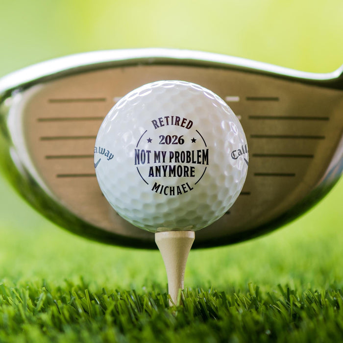 Close-up of a personalized retirement golf ball featuring a custom name and retirement year. Displayed on a tee with a golf club in the background.