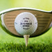 Close-up of a personalized retirement golf ball featuring a custom name and retirement year. Displayed on a tee with a golf club in the background.