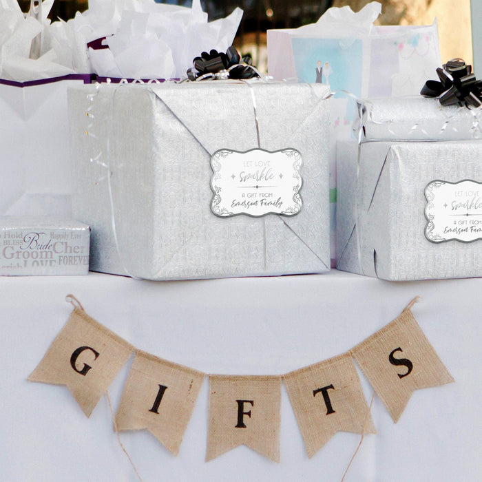 Silver wedding gift bag decorated with a personalized “Let Love Sparkle” gift tag in metallic silver foil. Styled with wedding décor and hanging banner accents for a romantic presentation.