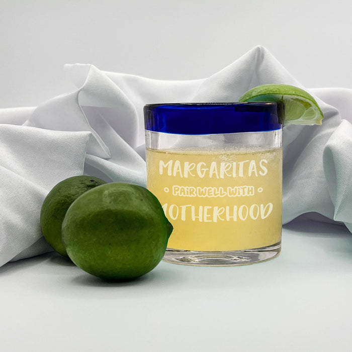 Engraved margarita glass displayed with fresh limes and white fabric behind it.