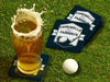 Custom square pulpboard coasters are shown sitting on a grassy, green golf course next to a pint of beer and a white golf ball. The pint of beer has a golf ball splashing into it and has a coaster underneath it. The coaster features design with an illustration of a golf ball and with club behind it and custom text.