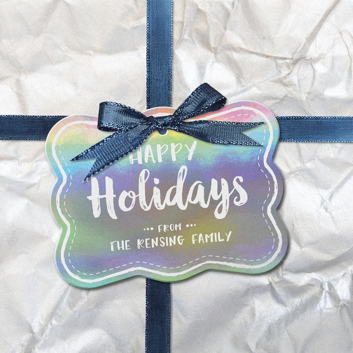 Rounded rectangle personalized Christmas hang tag attached to a white wrapped gift with a navy ribbon and bow.