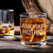 Lifestyle image of the whiskey glass with large ice cubes on a wooden table beside another drink. The “Ask Your Mother” design adds a fun and casual bar feel.